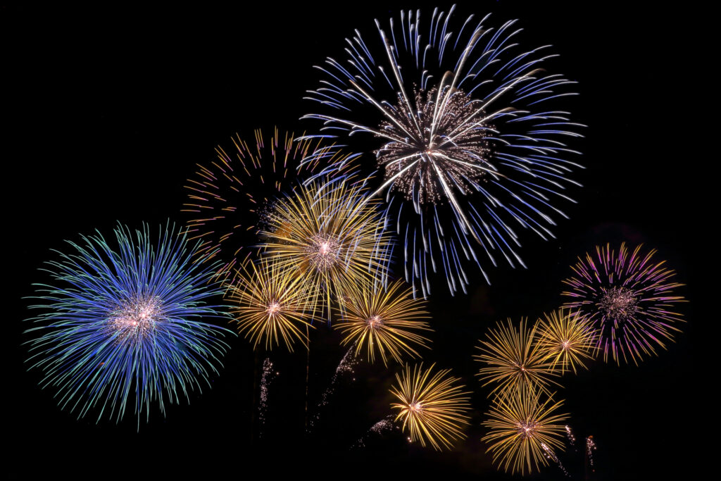 Colorful fireworks exploding in a dark night sky with blue, yellow, and purple bursts forming circular patterns.