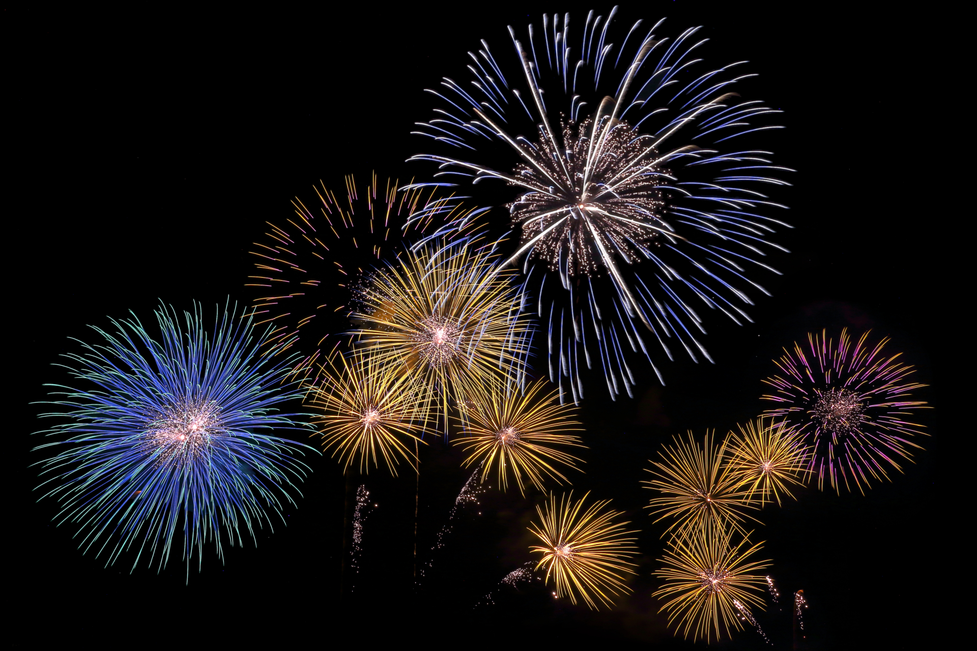 Colorful fireworks exploding in a dark night sky with blue, yellow, and purple bursts forming circular patterns.
